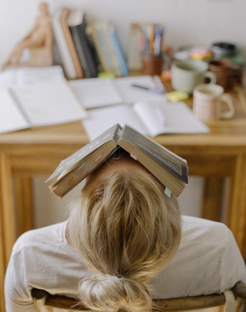 Niña Sentada En La Mesa Con Un Libro En La Frente